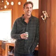 Man leaning against cabin wall with coffee in hand.