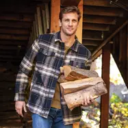 Man carrying wood logs outside cabin.